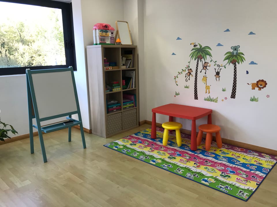 Rincón infantil de la consulta con mesa y taburetes de colores, pizarra y alfombra con letras